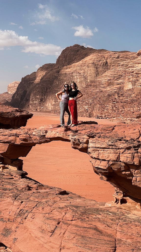 Two women posing on a naturally formed rock bridge in Wadi Rum Desert in Jordan.
