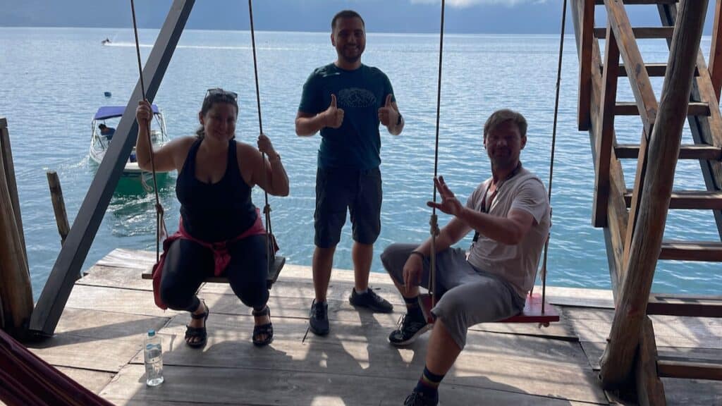 Three backpackers sitting on swings in front of a lake in El Salvador.