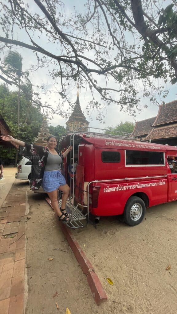 Traveler climbing into a red songthaew in Chiang Mai’s Old City near historic temples—an essential part of exploring local life and deciding where to stay in Chiang Mai, from the walkable Old City to trendy Nimman.